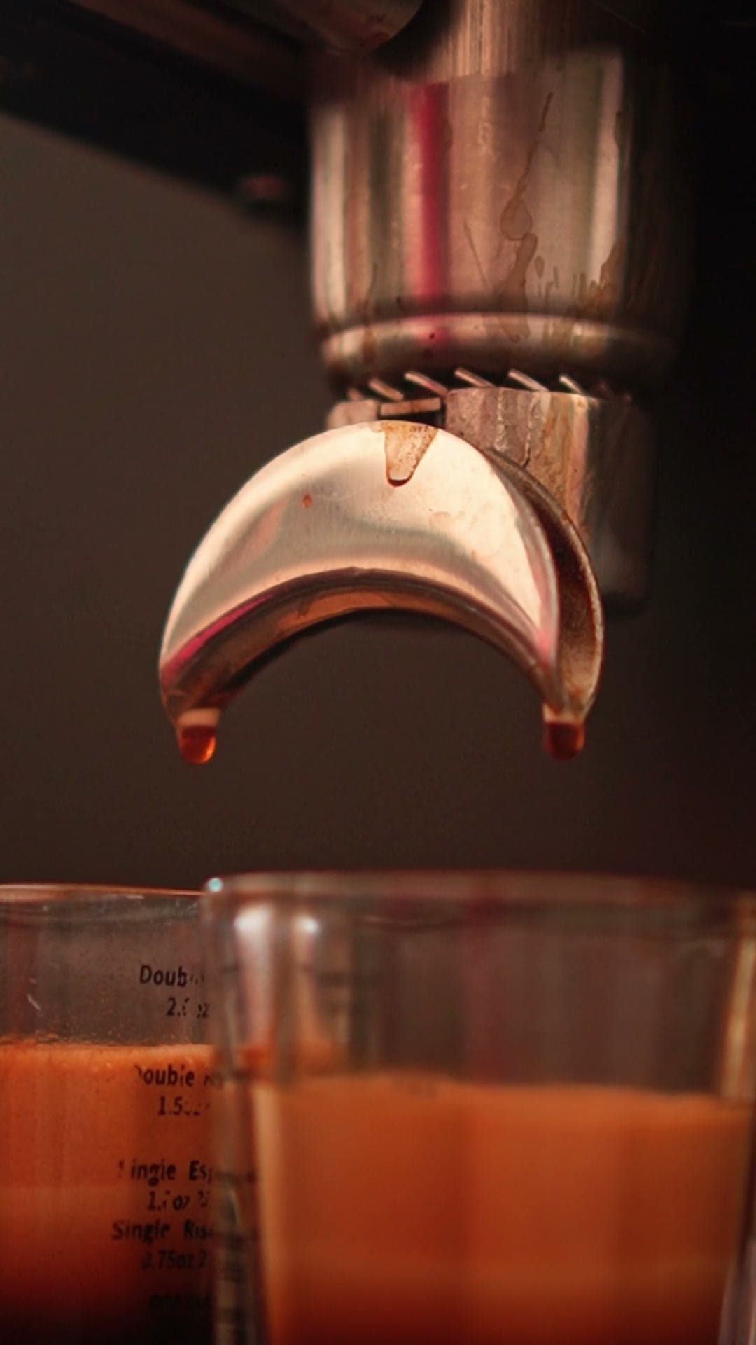 Espresso pouring from a portafilter into a shot glass, in warm cafe light.
